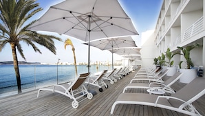 Een terras met ligbedden en parasols, met uitzicht op een waterpartij.