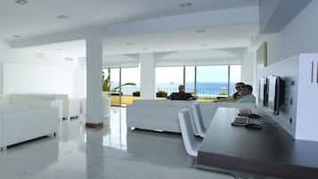 Un moderno vestíbulo de hotel con un sofá blanco, un escritorio con computadora y vistas al mar a través de amplios ventanales.