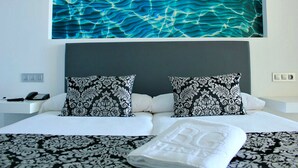 Een hotelkamer met een groot bed, twee gestreepte kussens, een nachtkastje met een telefoon en een kunstwerk aan de muur.