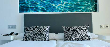 A hotel room with a large bed, two patterned pillows, a nightstand with a phone, and a wall art piece.