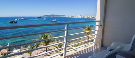 Un balcón con vista al mar, sillas blancas y suelo de baldosas.