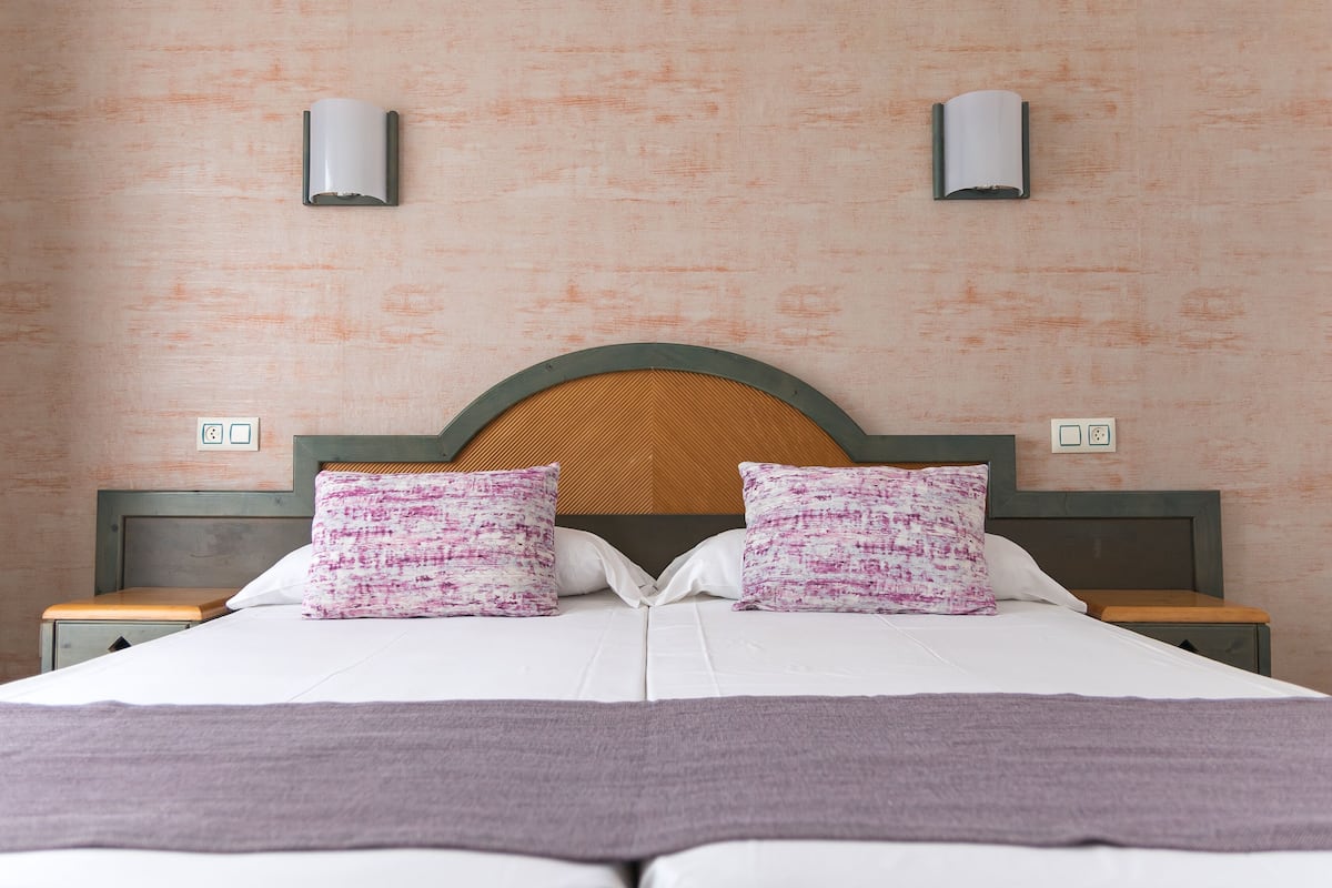 A bed with a wooden headboard, two pillows, a white bedspread, and two nightstands with lamps.