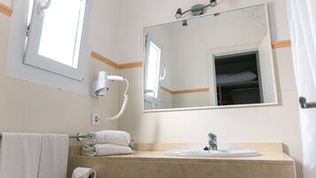 Un baño con lavamanos, espejo, toallero y ventana.