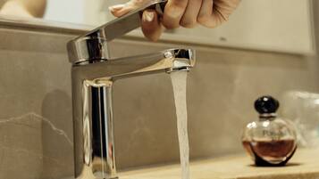 Una mano gira un grifo cromado moderno mientras el agua fluye hacia un lavabo color beige.