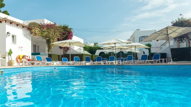 A swimming pool with blue water, surrounded by lounge chairs and umbrellas. - Hotel d´Or (Santanyi)