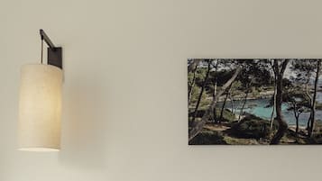 Un dormitorio con una cama, una mesita de noche con un teléfono, una lámpara y un cuadro con un paisaje.