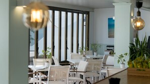 A modern dining area with white furniture, large windows, and potted plants. - Hotel d´Or (Santanyi)