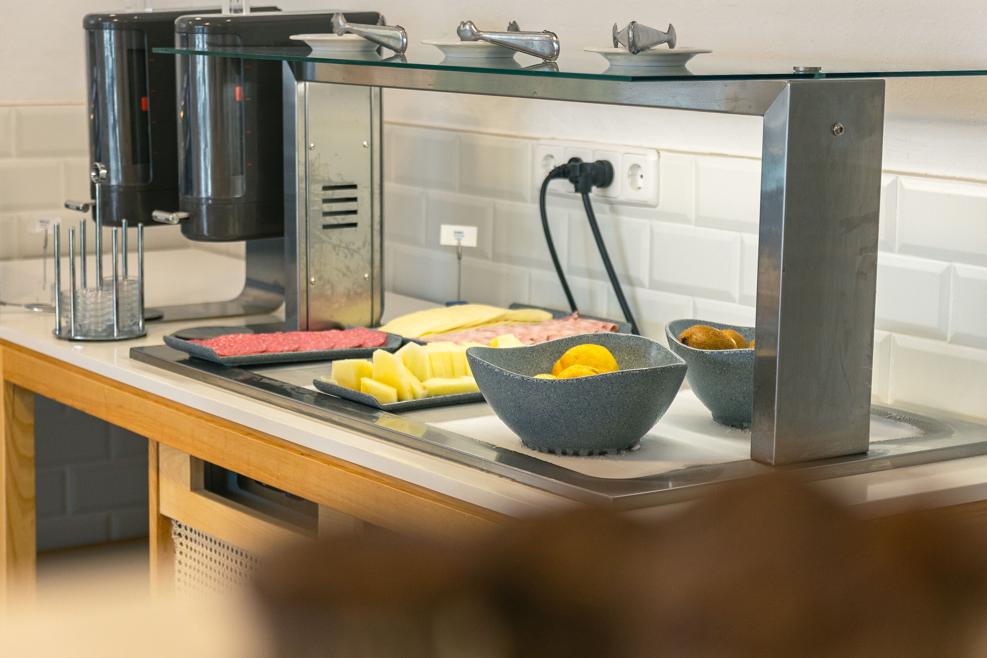 A breakfast bar with a coffee machine, a variety of food items including meats and fruits, and a bowl of lemons.