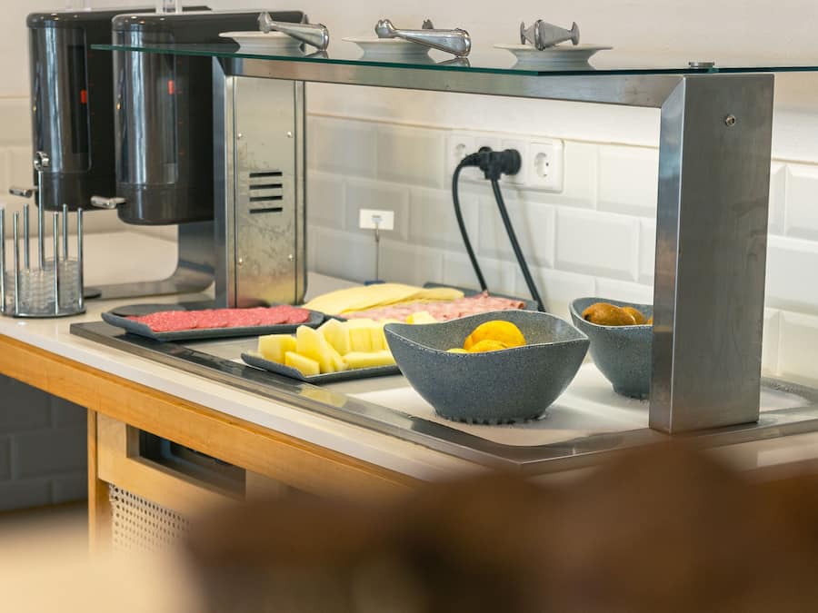 Una barra de desayuno con una máquina de café, diversas opciones de alimentos como carnes y frutas, y un bol de limones.