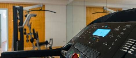 Un gimnasio con cinta de correr, equipo de ejercicio y una pantalla digital.