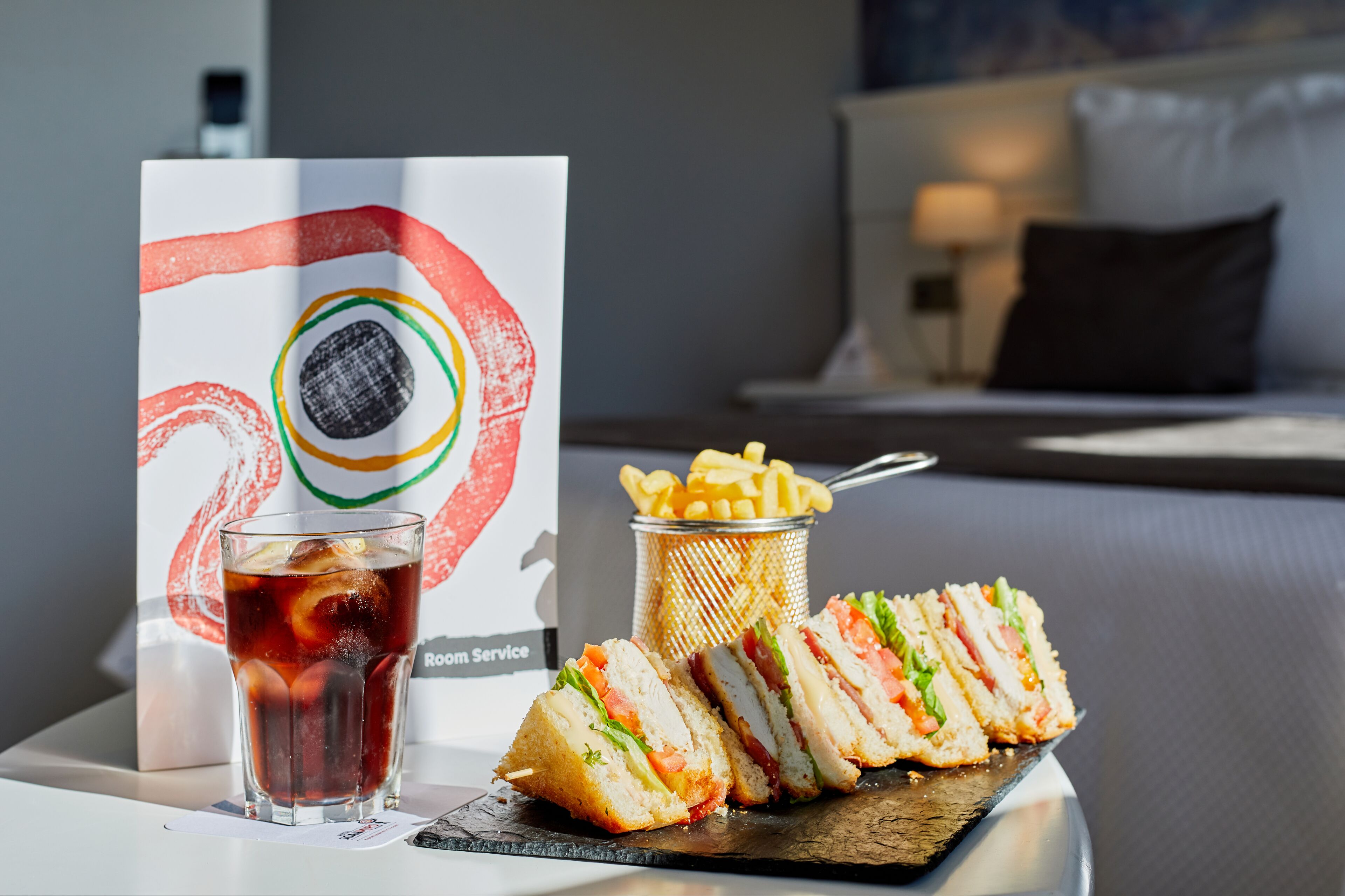 A sandwich, a drink, and a basket of fries on a table with a sign in the background.