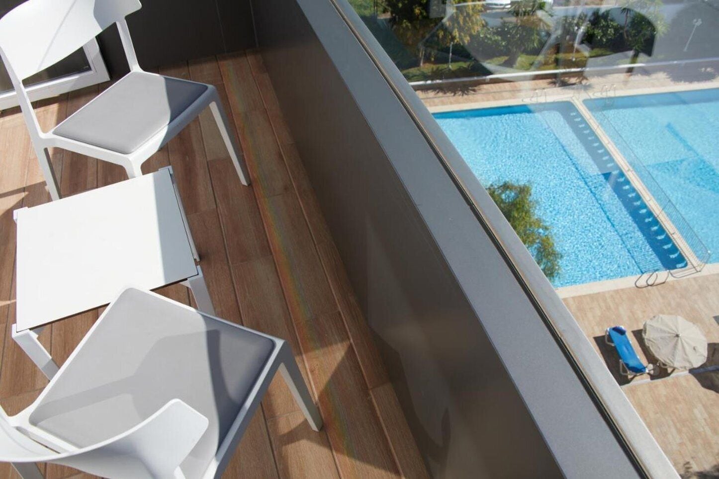 Un balcón con sillas blancas y vista a una piscina.