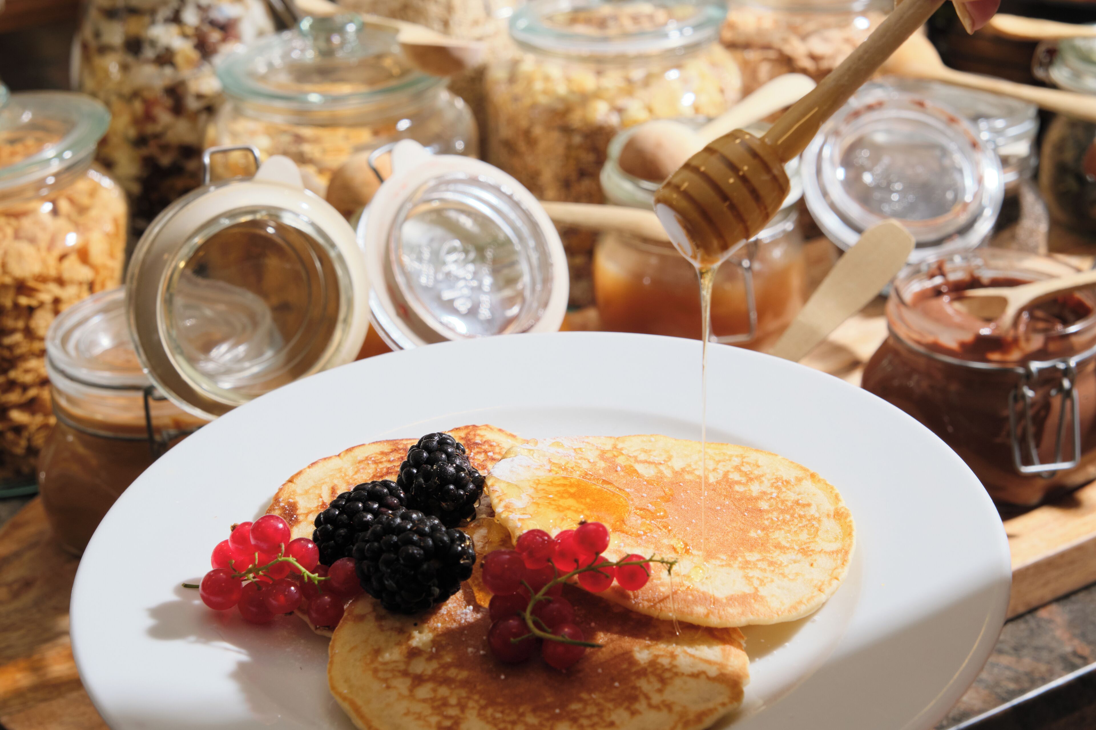 Un plato de desayuno con panqueques, frutos rojos y miel.