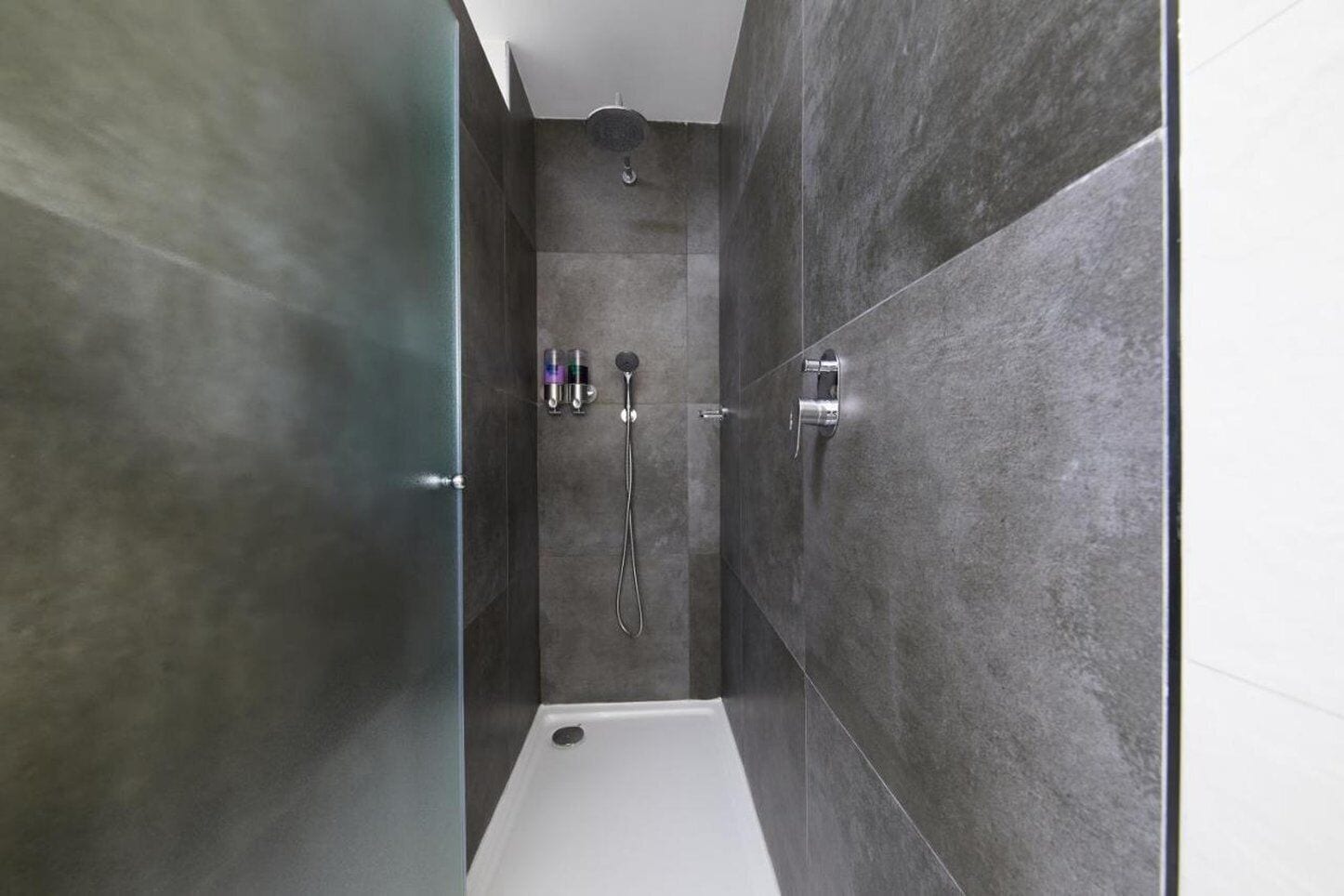 A modern shower area with a glass door, a handheld showerhead, and a wall-mounted faucet.