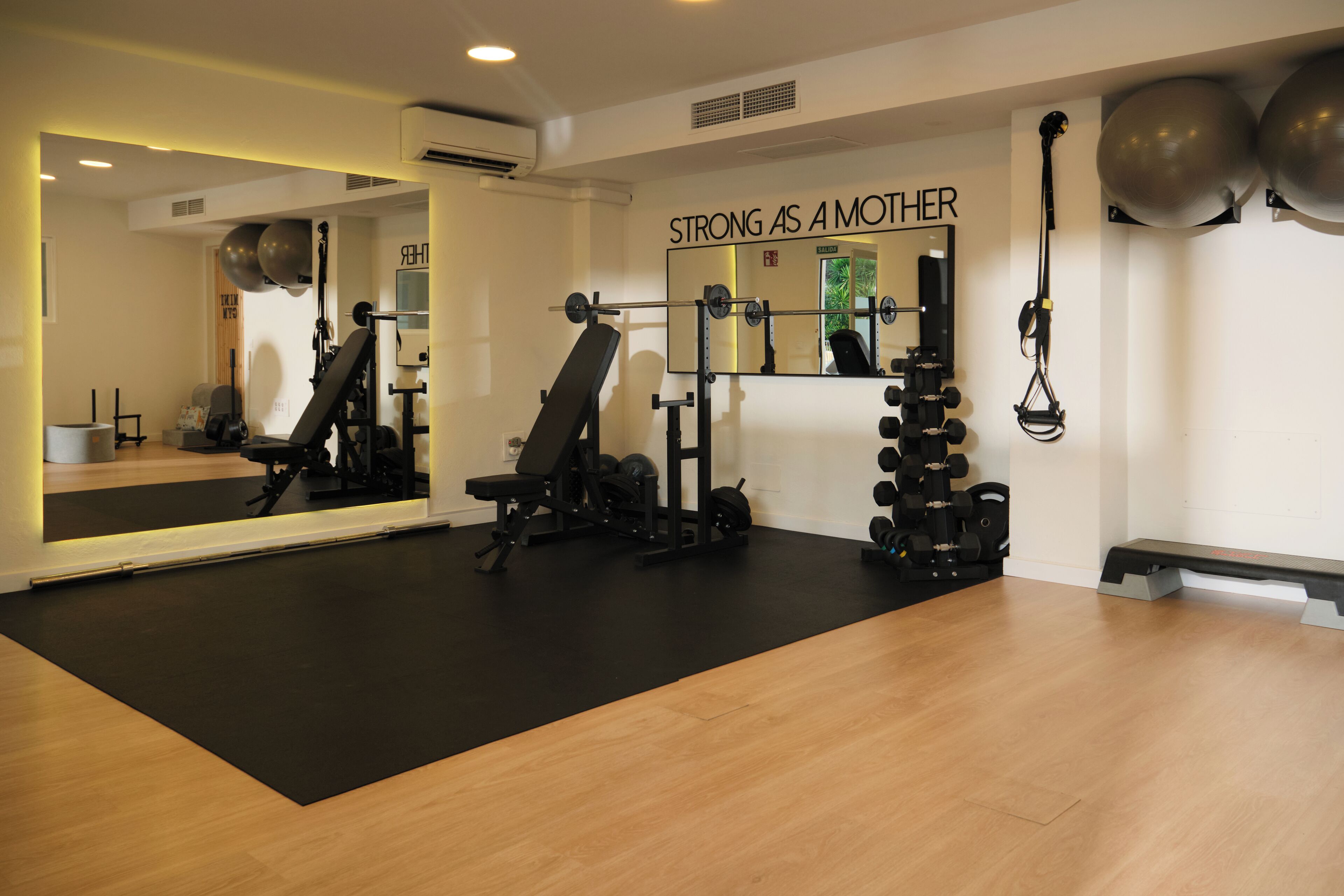 Una sala de gimnàstica amb equip d'exercici, un mirall i una frase motivacional a la paret.