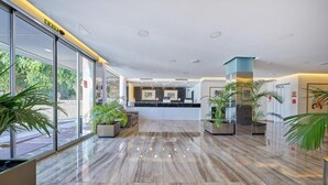 Un moderno vestíbulo de hotel con mostrador de recepción, puertas de cristal y plantas en macetas.