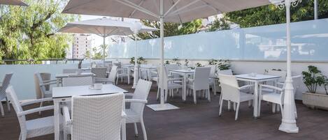 Un patio al aire libre con muebles de mimbre blanco y grandes sombrillas.