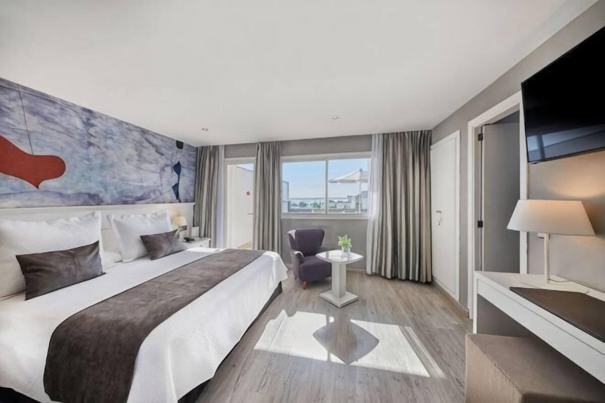 Habitación de hotel con una cama grande, televisión, una mesita y vistas a la ciudad.