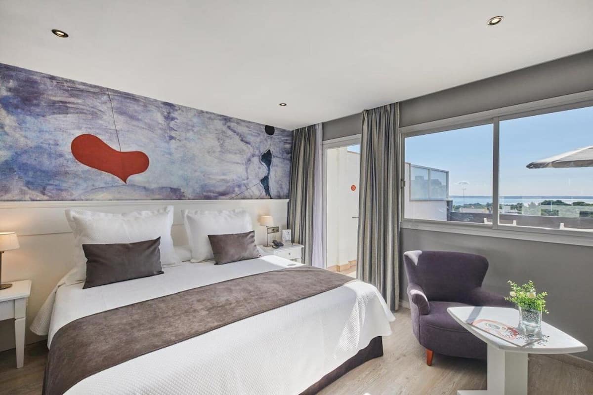 Habitación de hotel moderna con una cama grande, vista a la ciudad y un cuadro en la pared.