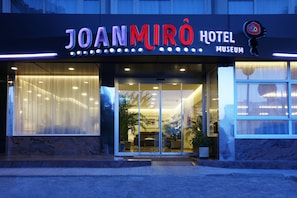 Exterior del Hotel Museo Joan Miró, con fachada moderna, amplia entrada de vidrio y visible zona de estar interior.