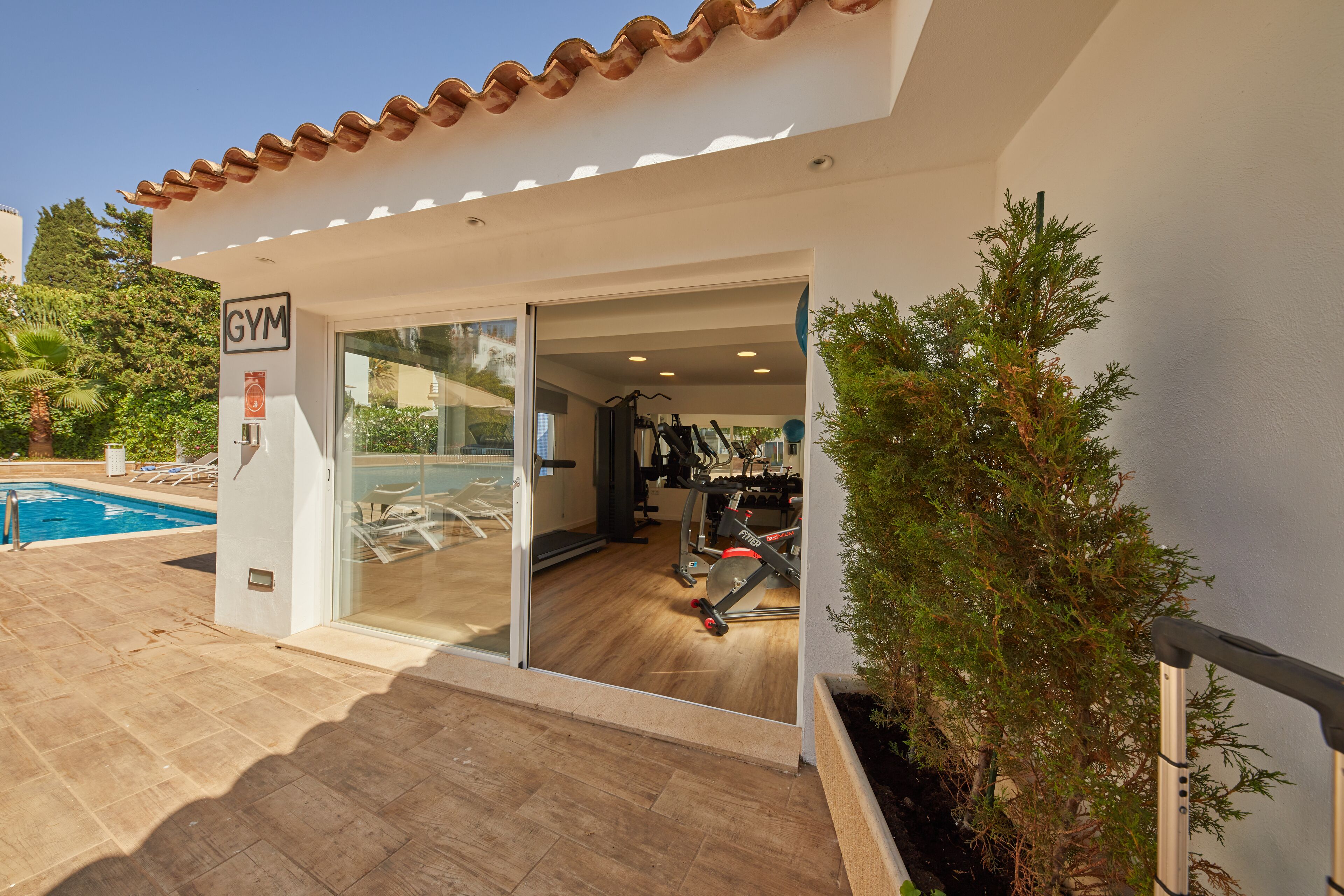 Une salle de sport avec une piscine, des appareils d’exercice et une porte en verre transparent.