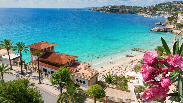 Un pueblo costero con playa, mar azul cristalino y edificios con tejados rojos.