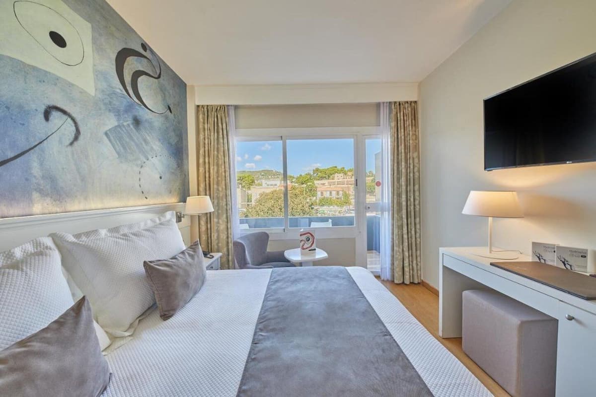 Habitación de hotel con una cama grande, un escritorio, un televisor y un balcón con vista a la ciudad.
