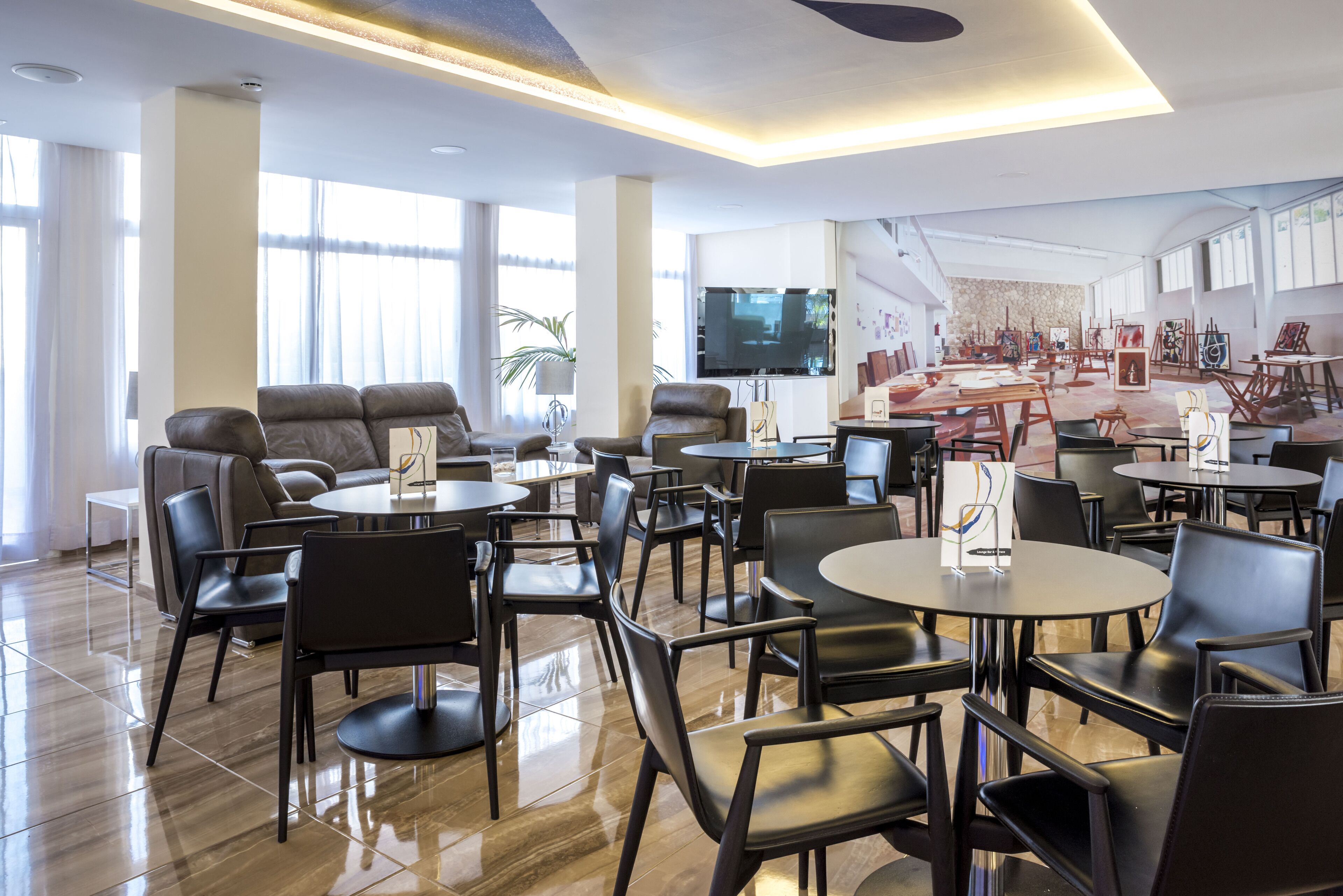 A spacious hotel lobby with multiple seating areas, a large flat-screen TV, and artwork on the walls.