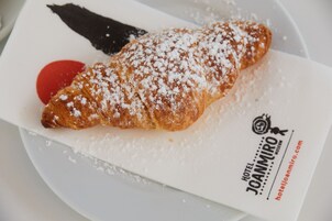 Un croissant espolvoreado con azúcar glas sobre un plato blanco con un logo y texto.