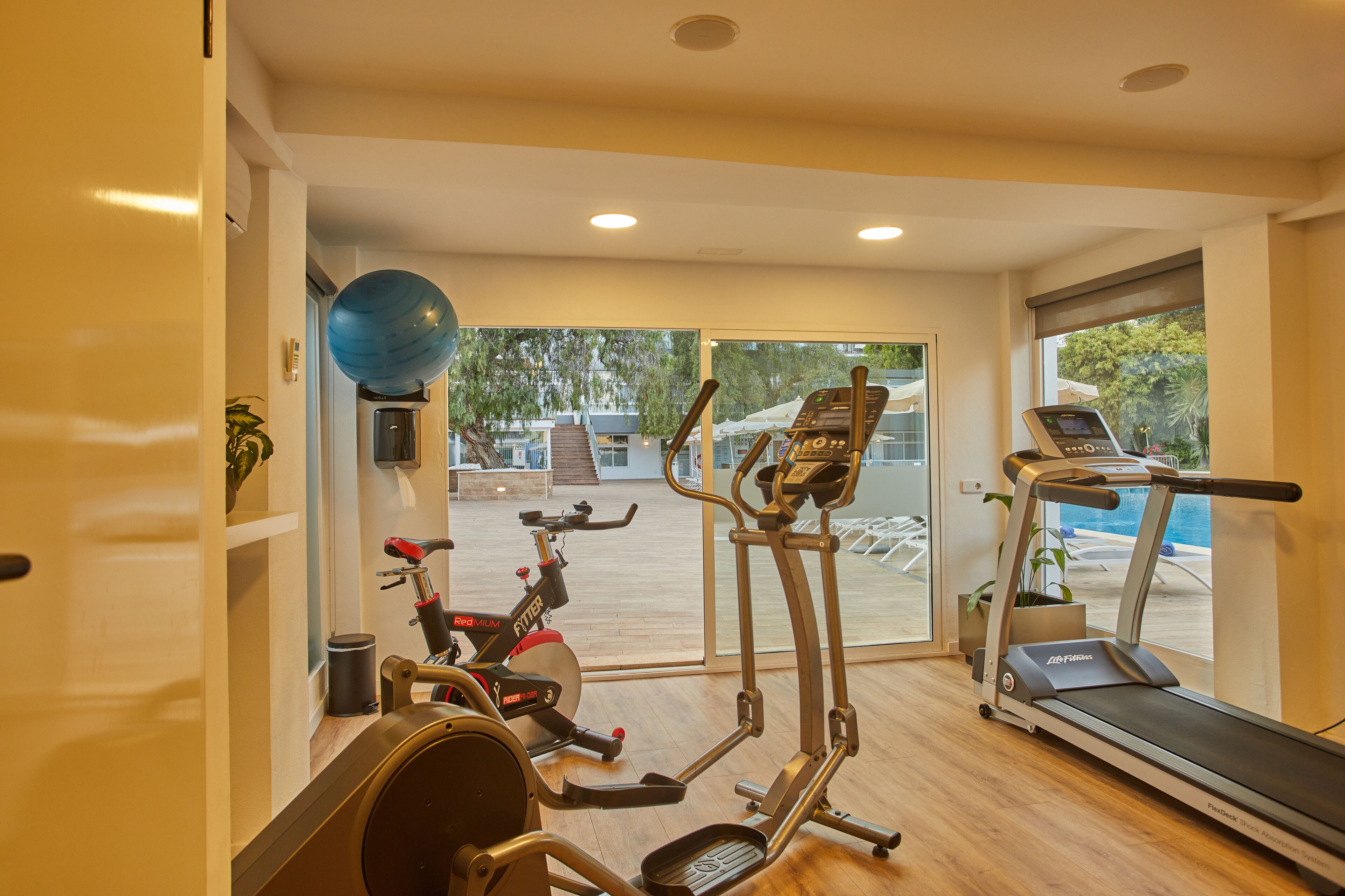 A home gym with an elliptical, a stationary bike, a treadmill, and a blue exercise ball.