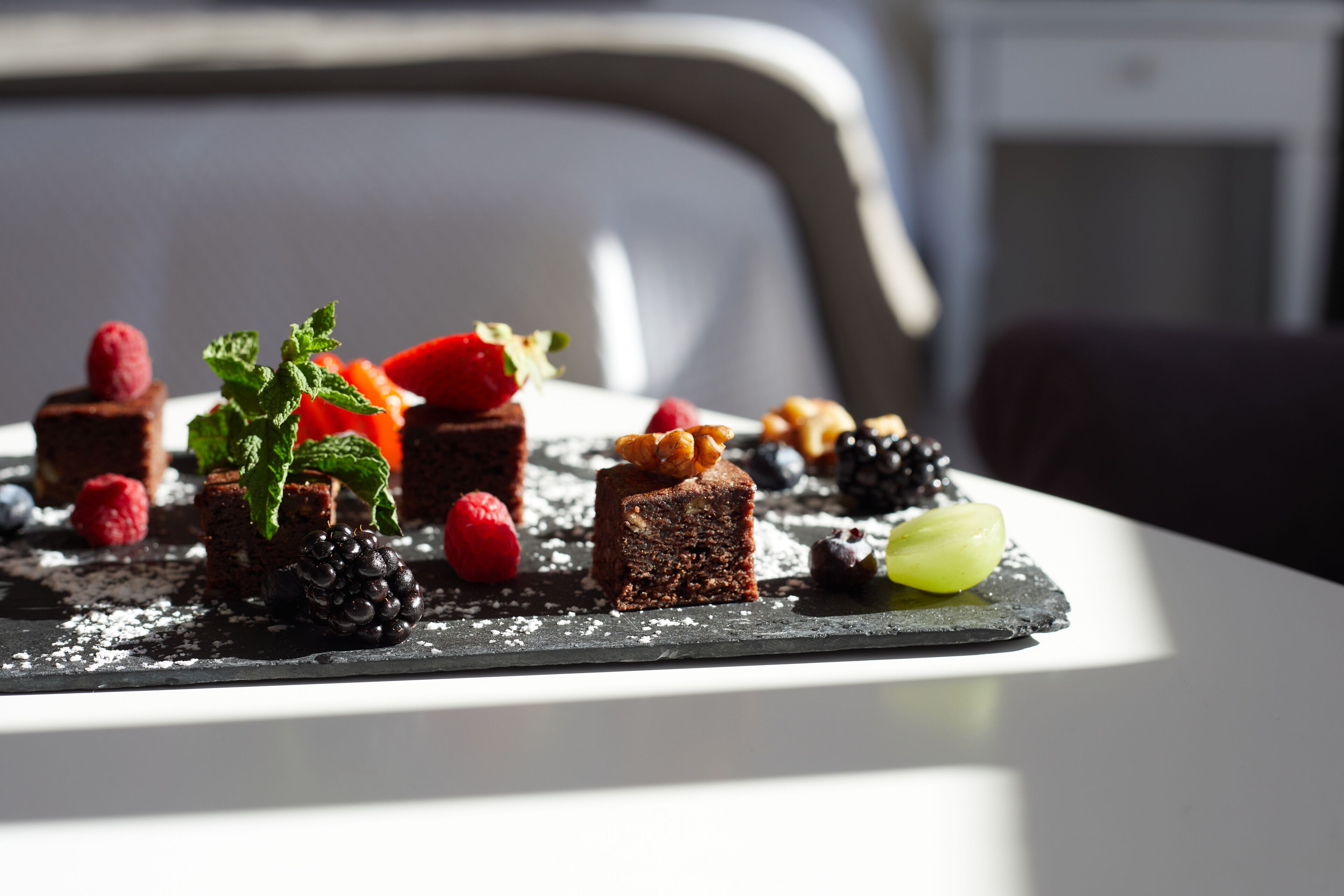 A dessert plate with various fruits and a mint leaf on a slate serving board.