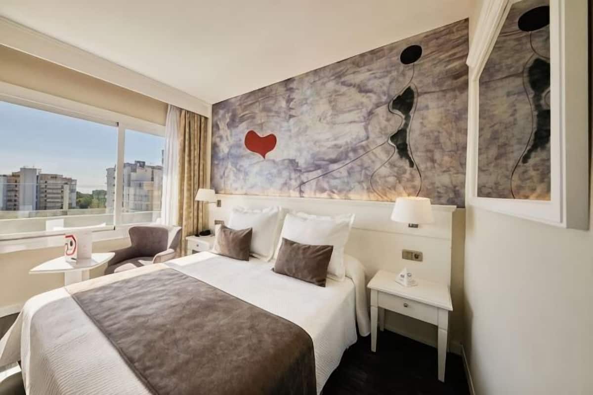 Una habitación de hotel con una cama grande, mesitas de noche, un escritorio y una silla.