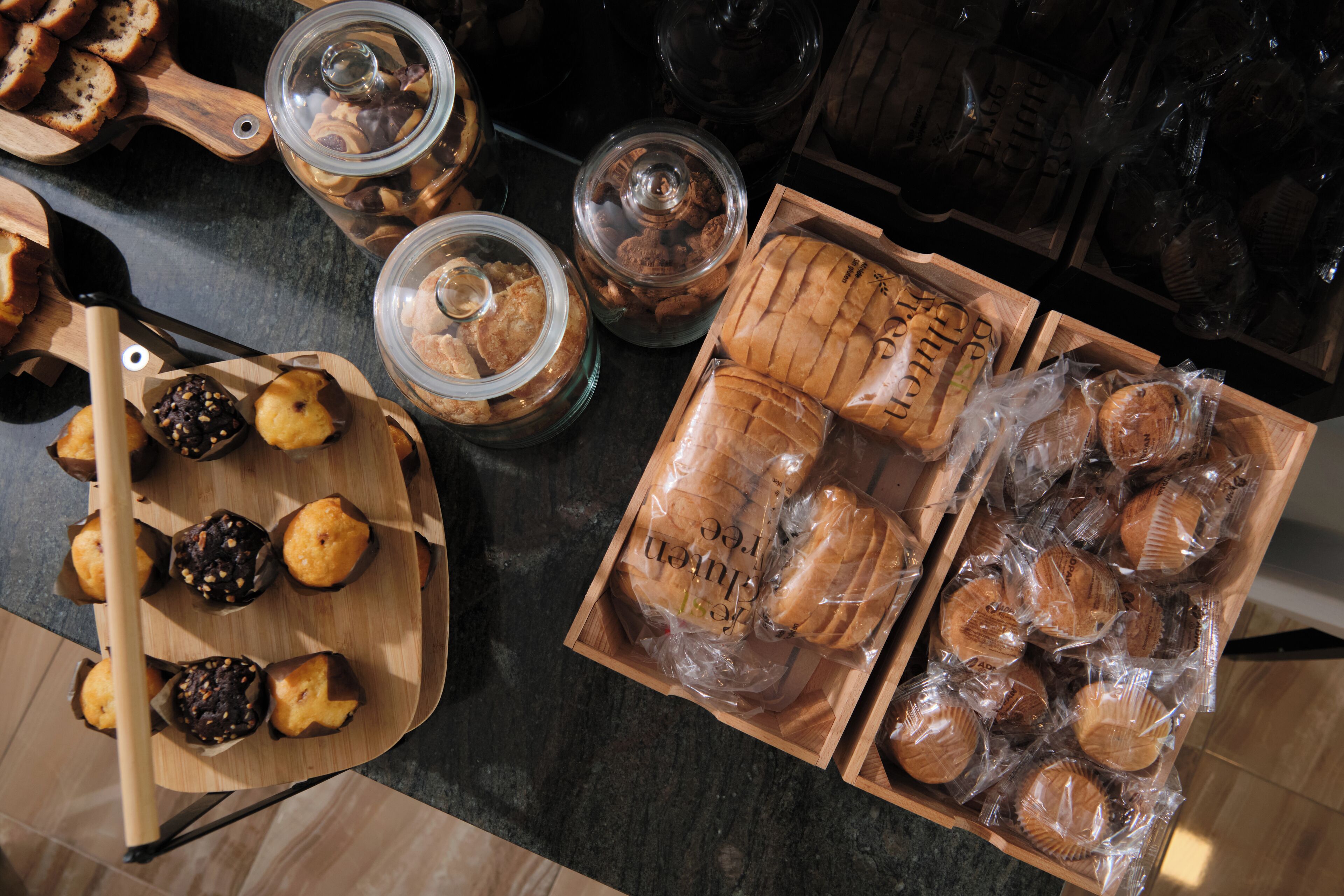 Variedad de productos horneados, como muffins y panes, expuestos en tablas de madera y frascos de vidrio.