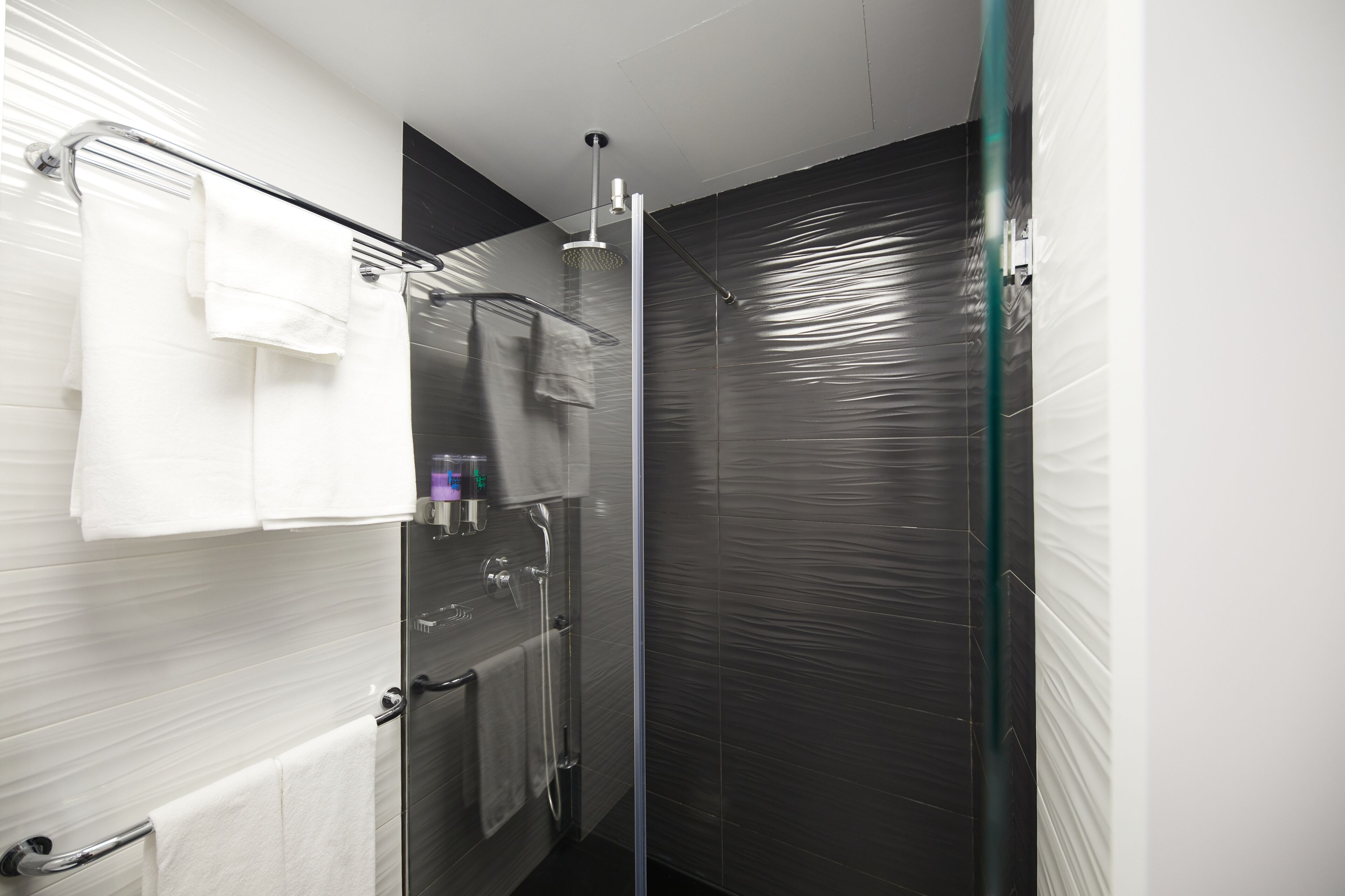 Un baño moderno con cabina de ducha de vidrio, un perchero blanco y una puerta de vidrio.