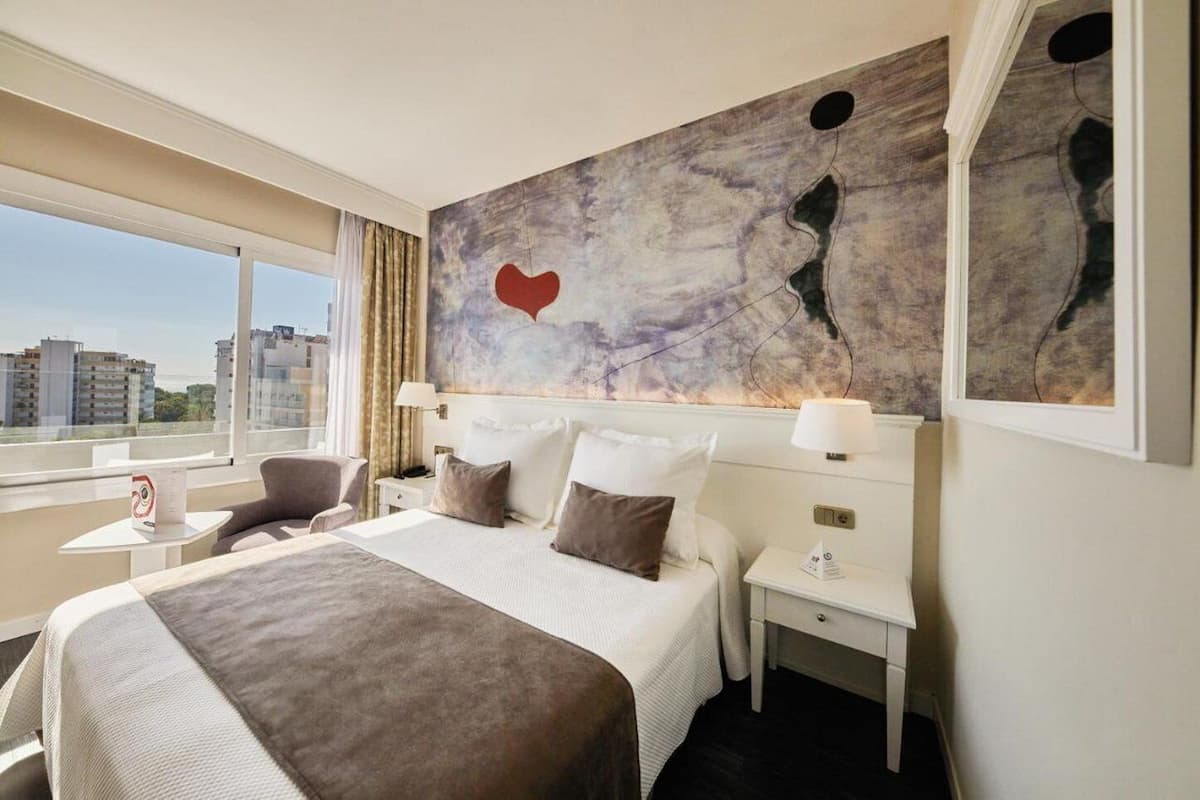 Habitación de hotel con una cama grande, un escritorio, una silla y vistas a la ciudad.