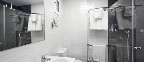 Un baño moderno con un espejo grande, baldosas blancas, un lavabo, inodoro y zona de ducha con mampara de vidrio.
