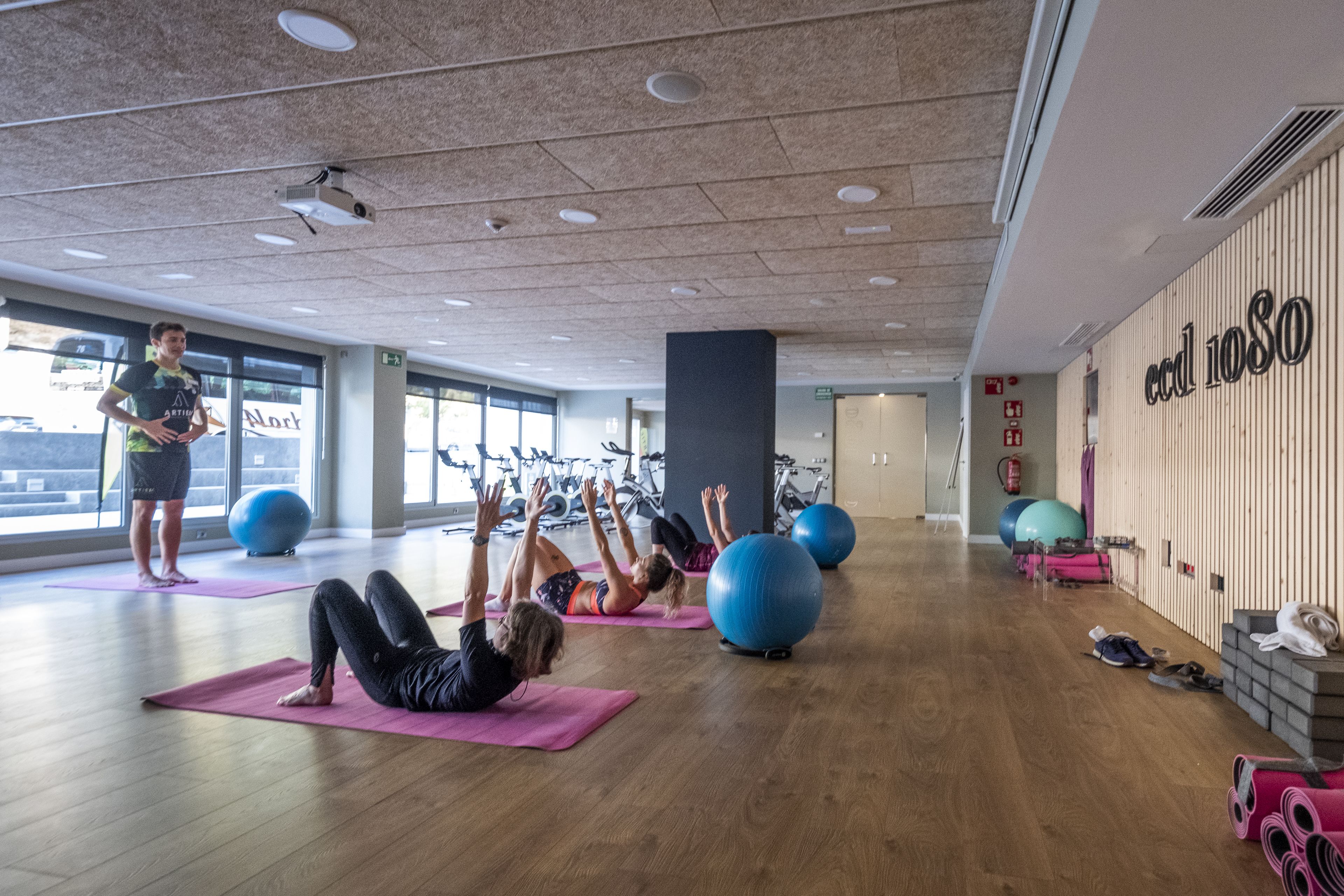 A gym with exercise balls, yoga mats, and a person standing.