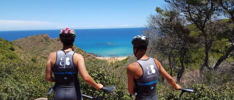 Two cyclists on a mountain bike trail overlooking a beach.
