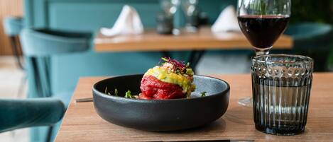 A bowl of food on a wooden table with a glass of red wine beside it.