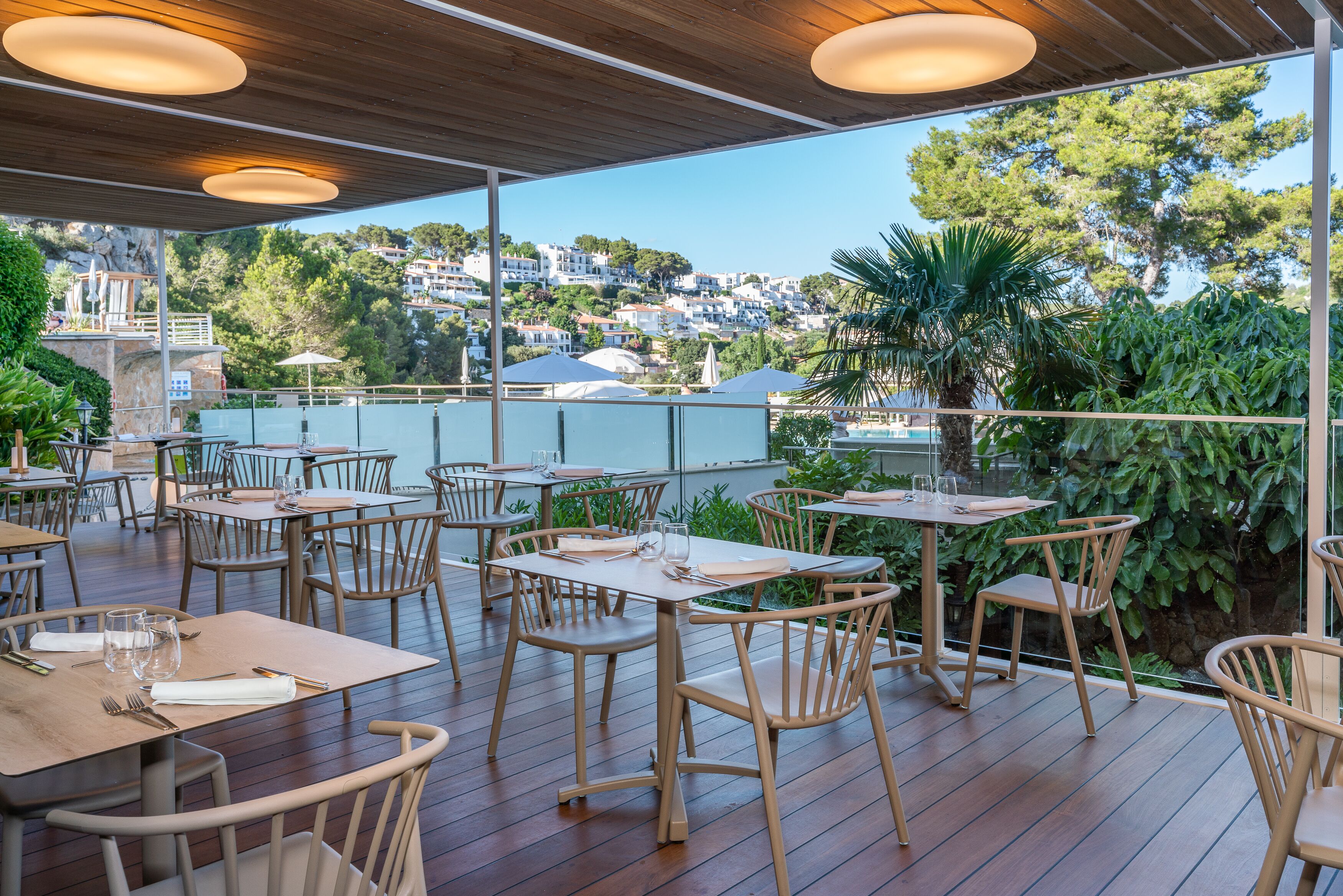 Un área de comedor al aire libre con mesas y sillas de madera, con vistas a una ladera panorámica.