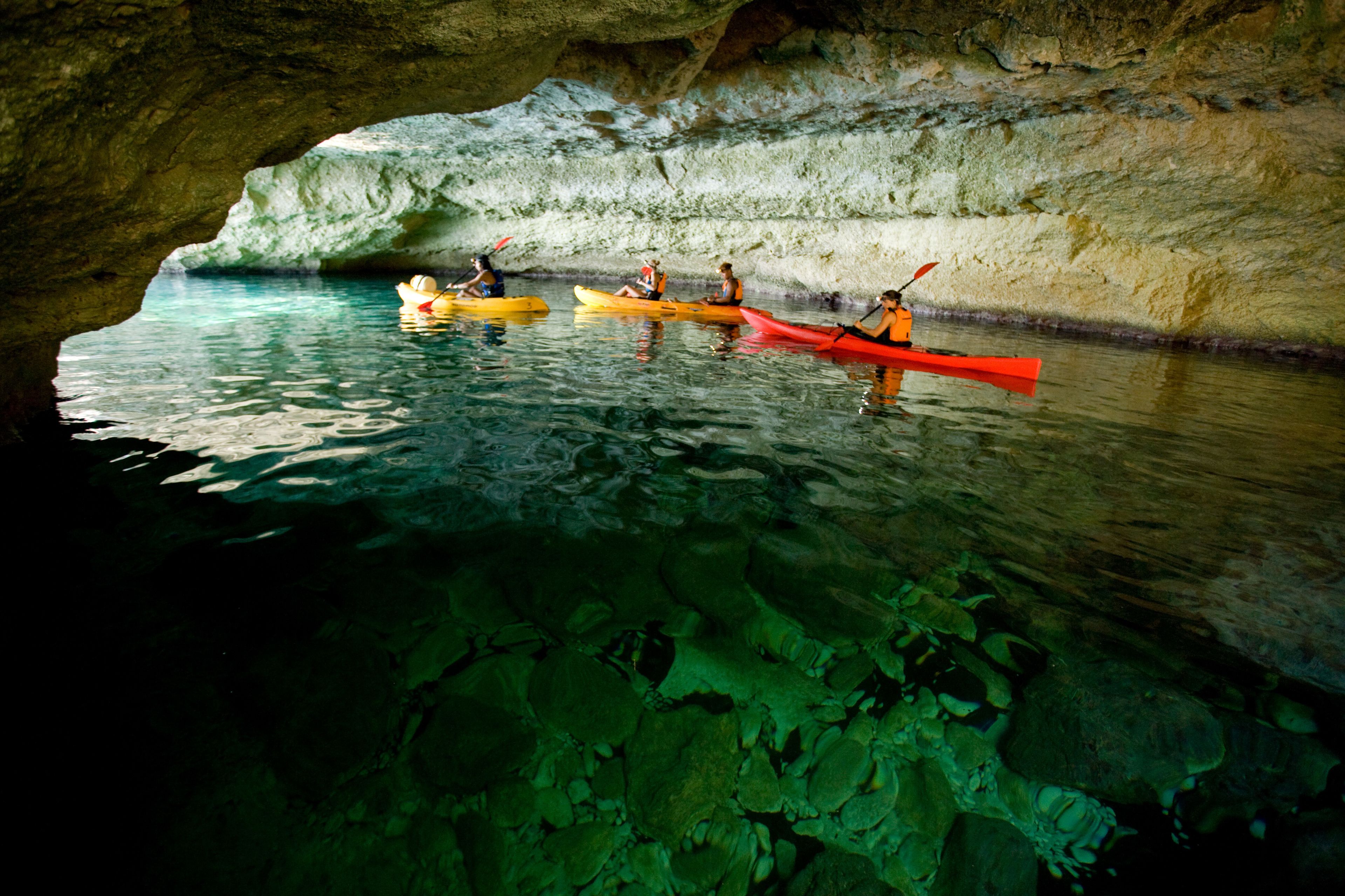 A cave with clear water and kayakers in yellow and red kayaks.