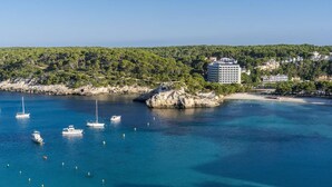 Une zone côtière comprenant un hôtel, des eaux d’un bleu limpide, des bateaux et un promontoire rocheux.