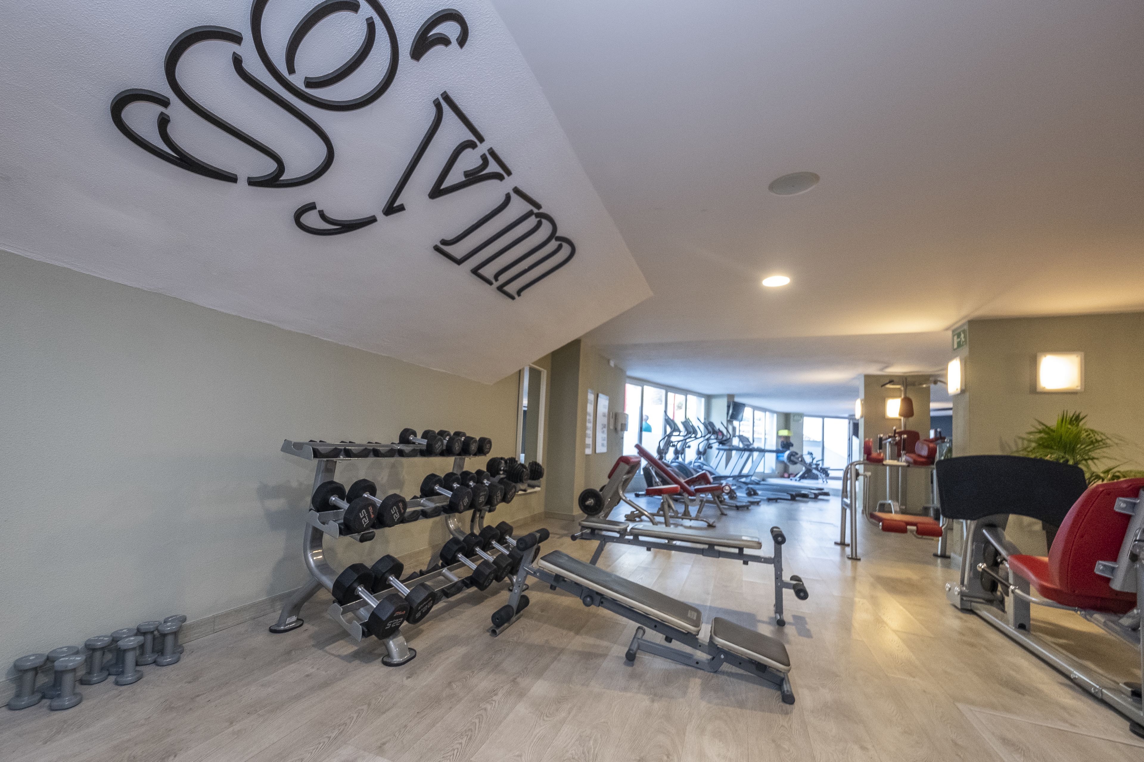 A gym with various exercise equipment, including dumbbells, a bench press, and cardio machines.
