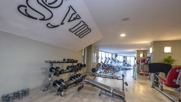 Een sportschool met diverse fitnessapparaten, waaronder gewichten, een bankdrukapparaat en cardio-apparaten.