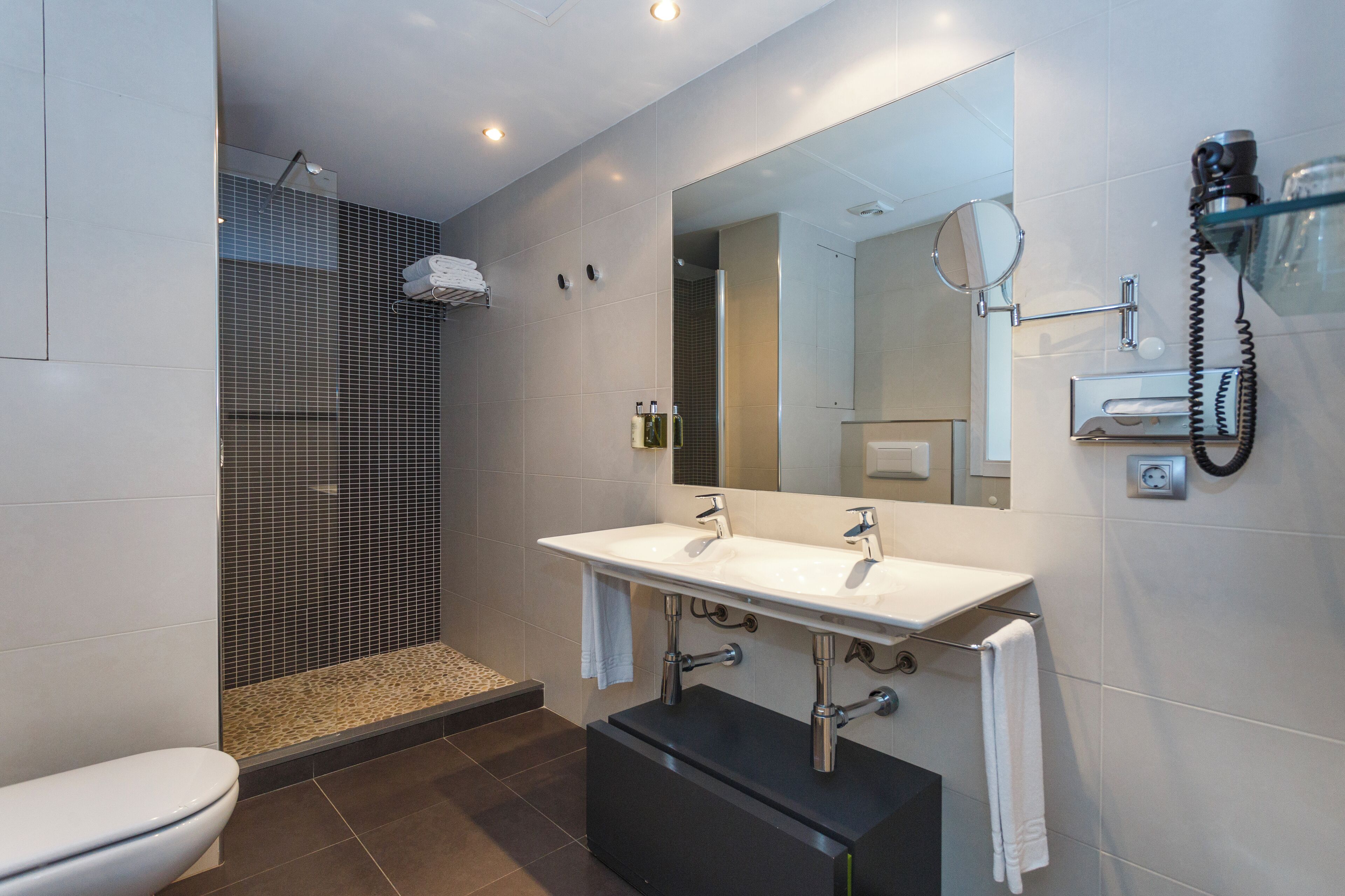 A modern bathroom with a shower, toilet, and vanity with a large mirror.