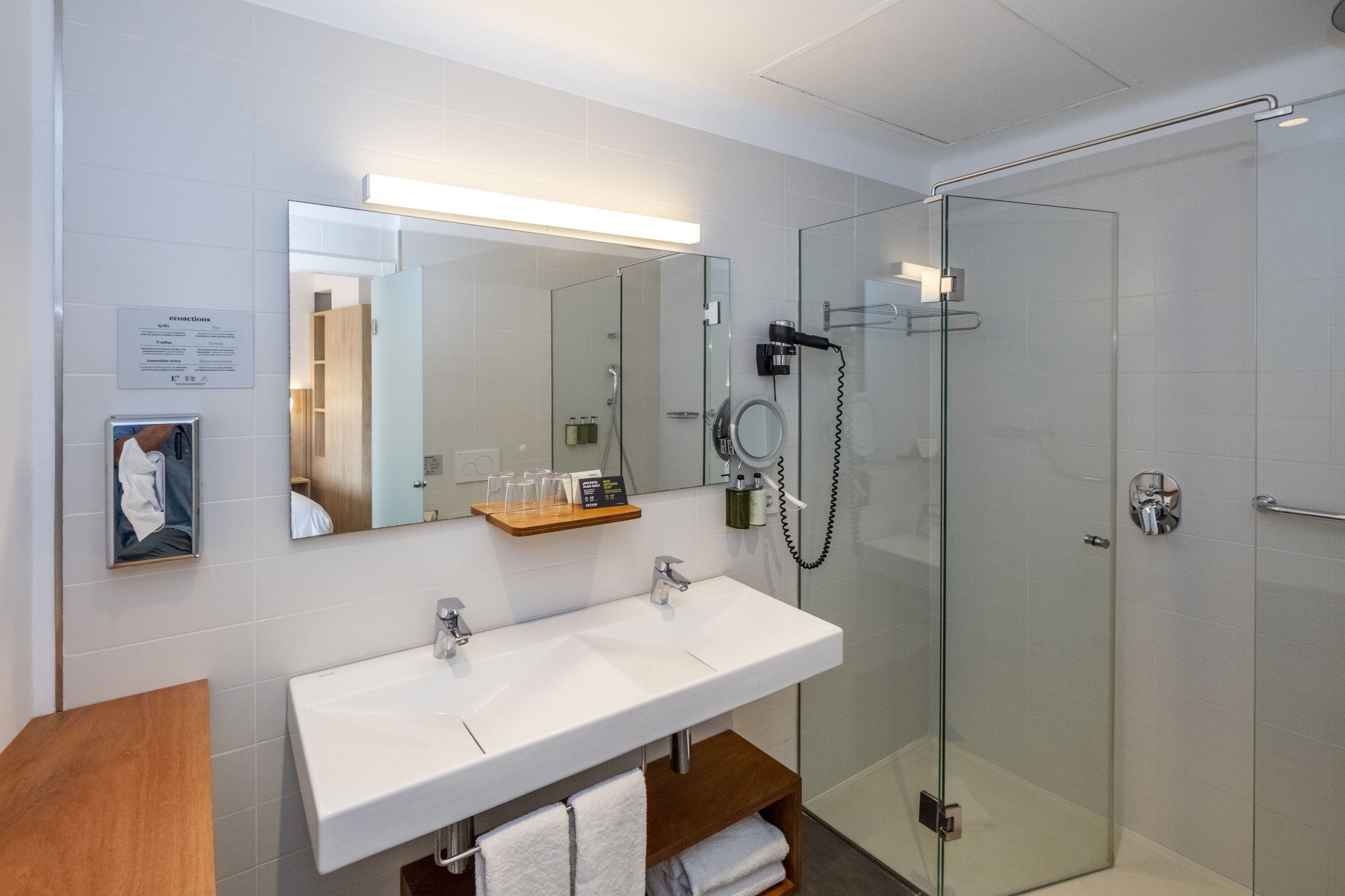 Un baño moderno con cabina de ducha de vidrio, tocador doble y espejo sobre el lavabo.