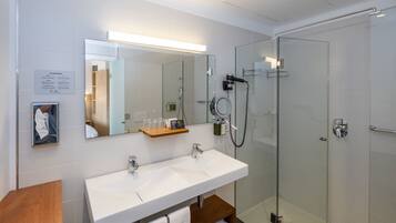 Un baño moderno con cabina de ducha de vidrio, tocador doble y espejo sobre el lavabo.