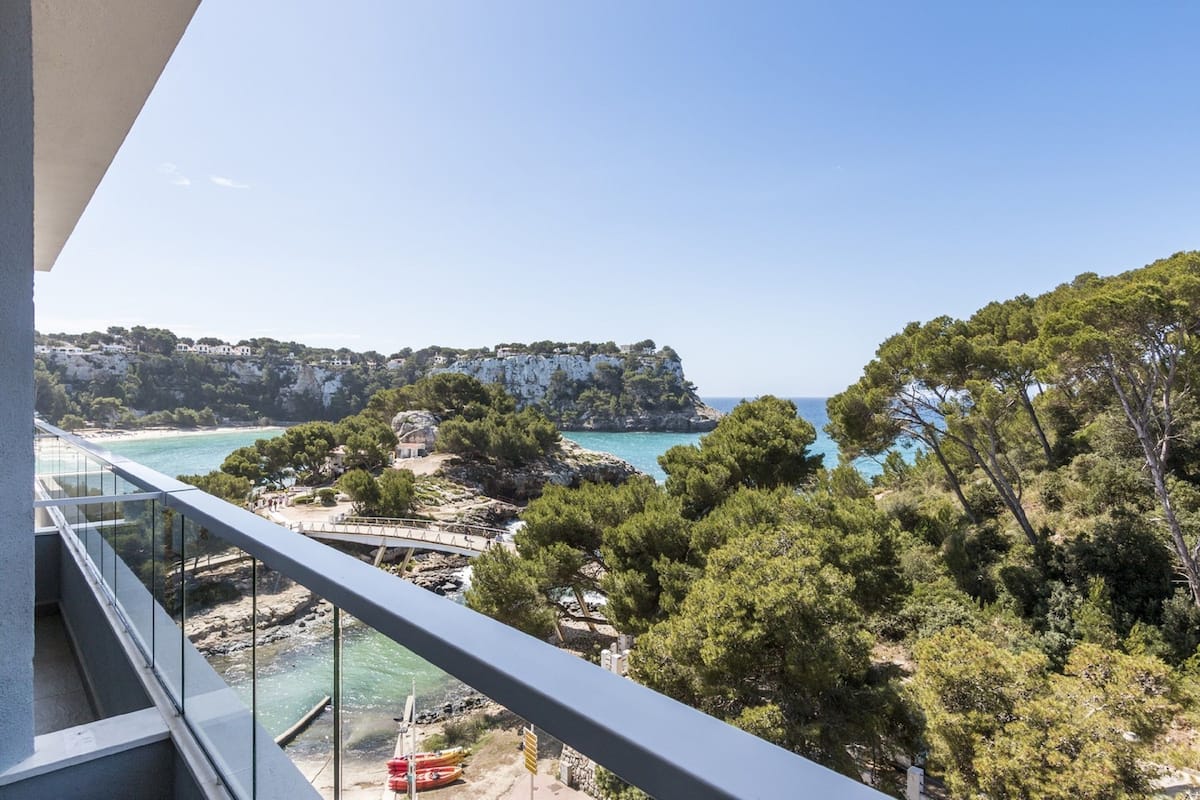 Un balcon offrant une vue dégagée sur un paysage côtier, comprenant des falaises rocheuses, une plage et un pont.