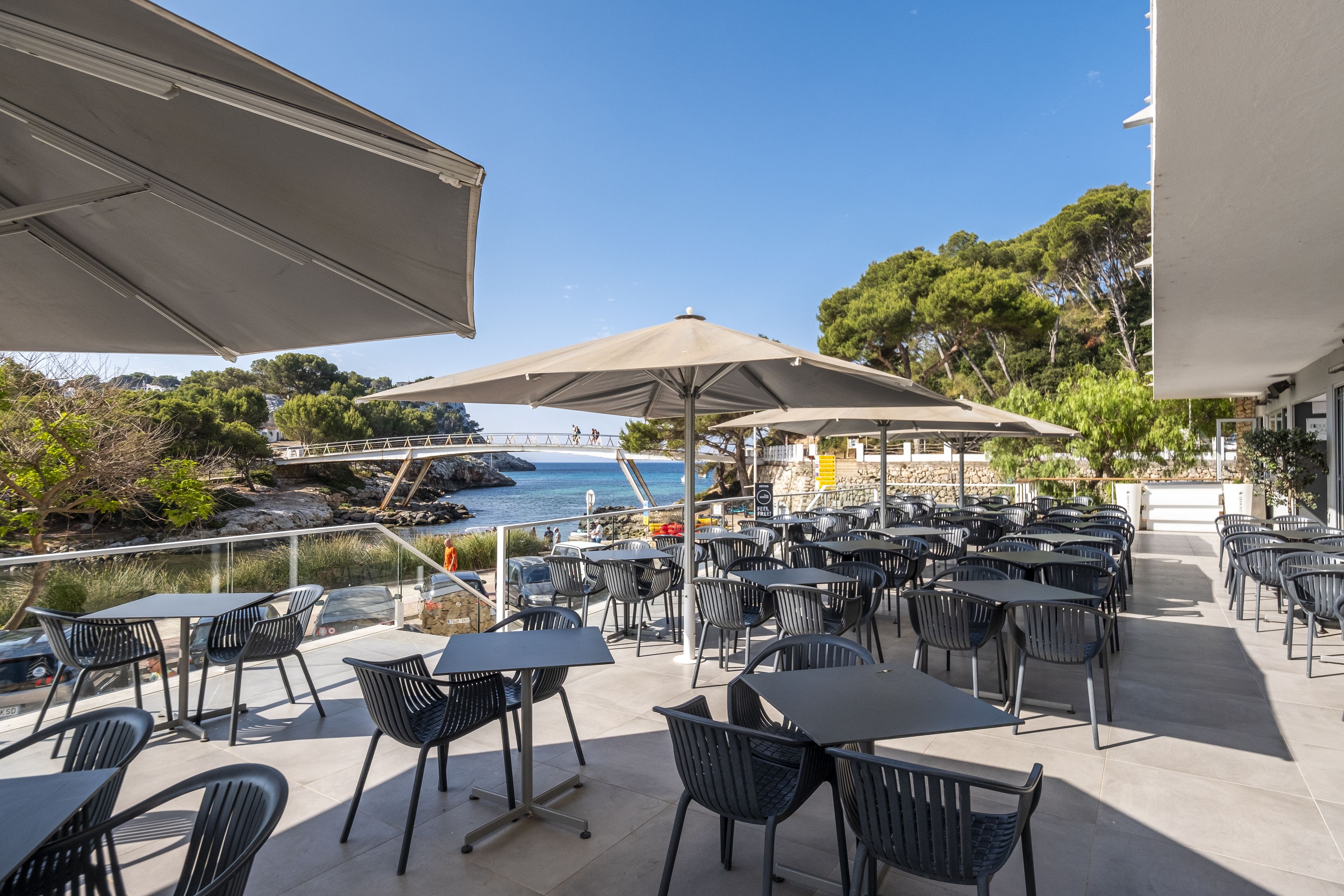 An outdoor patio with tables and chairs, overlooking a rocky coastline and a bridge.