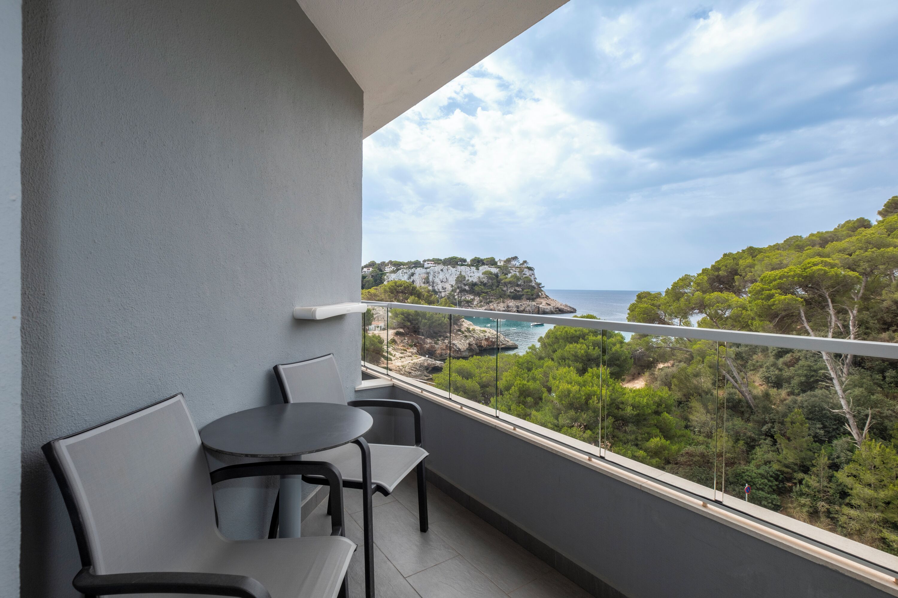 Ein Balkon mit Tisch und Stühlen mit Blick auf eine Küstenlandschaft mit Bäumen und Klippen.
